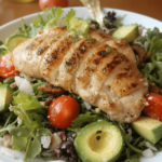 A vibrant Grilled Chicken & Avocado Salad with juicy grilled chicken, creamy avocado, cherry tomatoes, and mixed greens, drizzled with a tangy dressing.